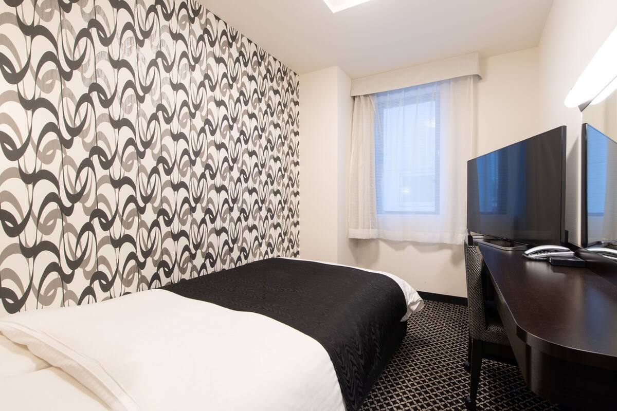 Habitación de hotel con cama, escritorio con computadora, televisor y ventana con cortinas.