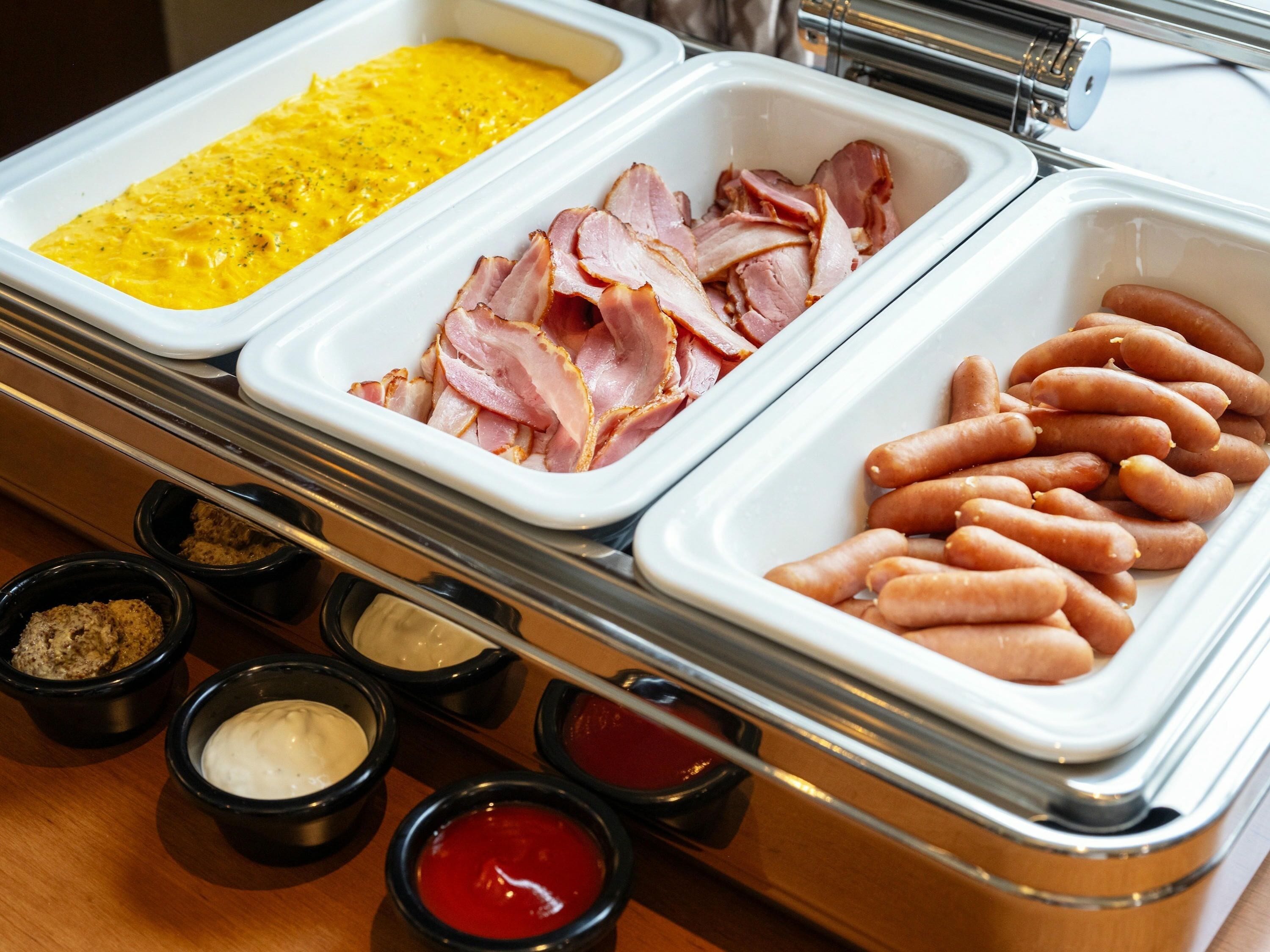 Een buffet met diverse gerechten, waaronder ham, worst en een gele spread.