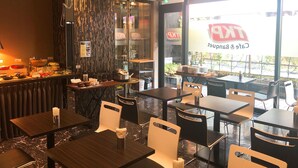 Interior de un restaurante con mesas, sillas, una barra con alimentos y vistas a la calle.
