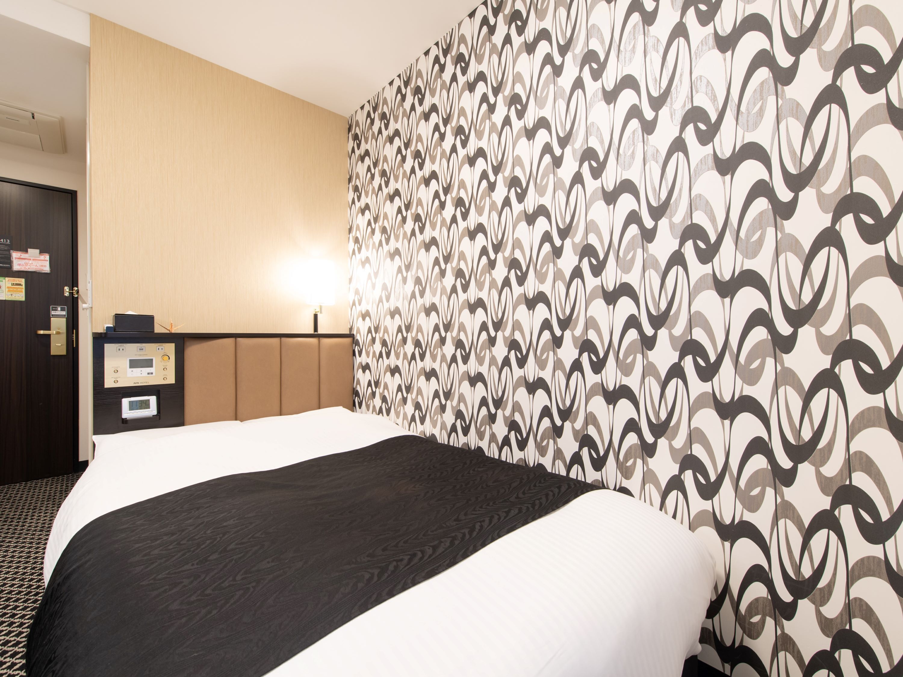 Habitació d'hotel amb un llit, un panell de control, un escriptori i una paret amb un disseny.