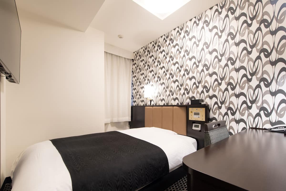 Habitación de hotel con cama, escritorio, teléfono y panel de control.