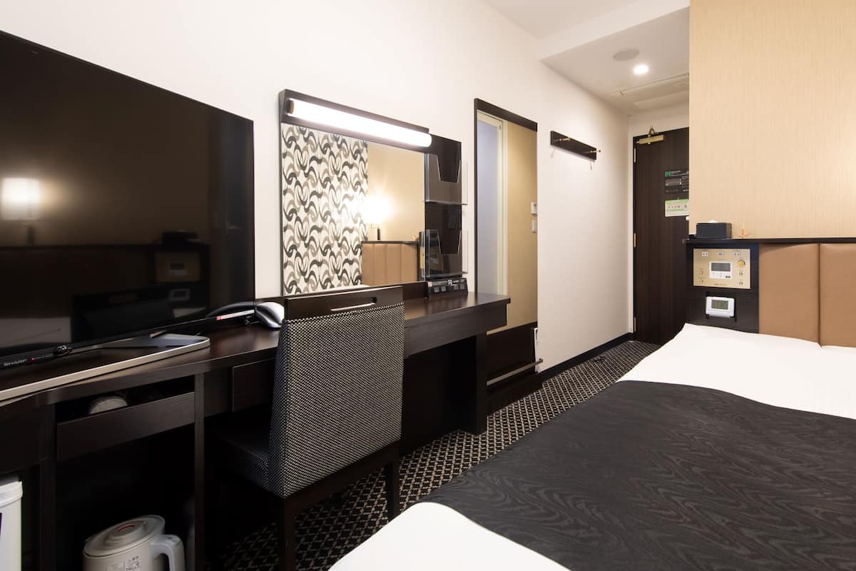 Habitación de hotel con escritorio, silla, cama y espejo.