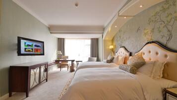 A hotel room with two beds, a TV on the wall, a desk with a chair, and a large window.
