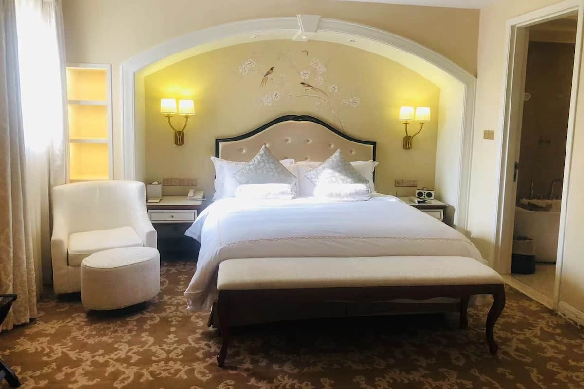 Una habitación de hotel con una cama grande, dos lámparas de noche, una silla y una mesita.