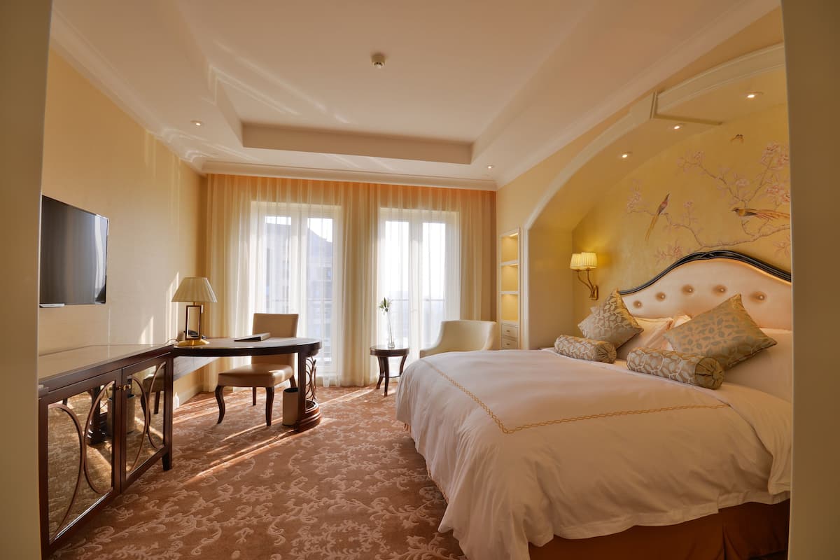 Habitación de hotel con una cama grande, un escritorio, una silla, un televisor y una ventana con cortinas.