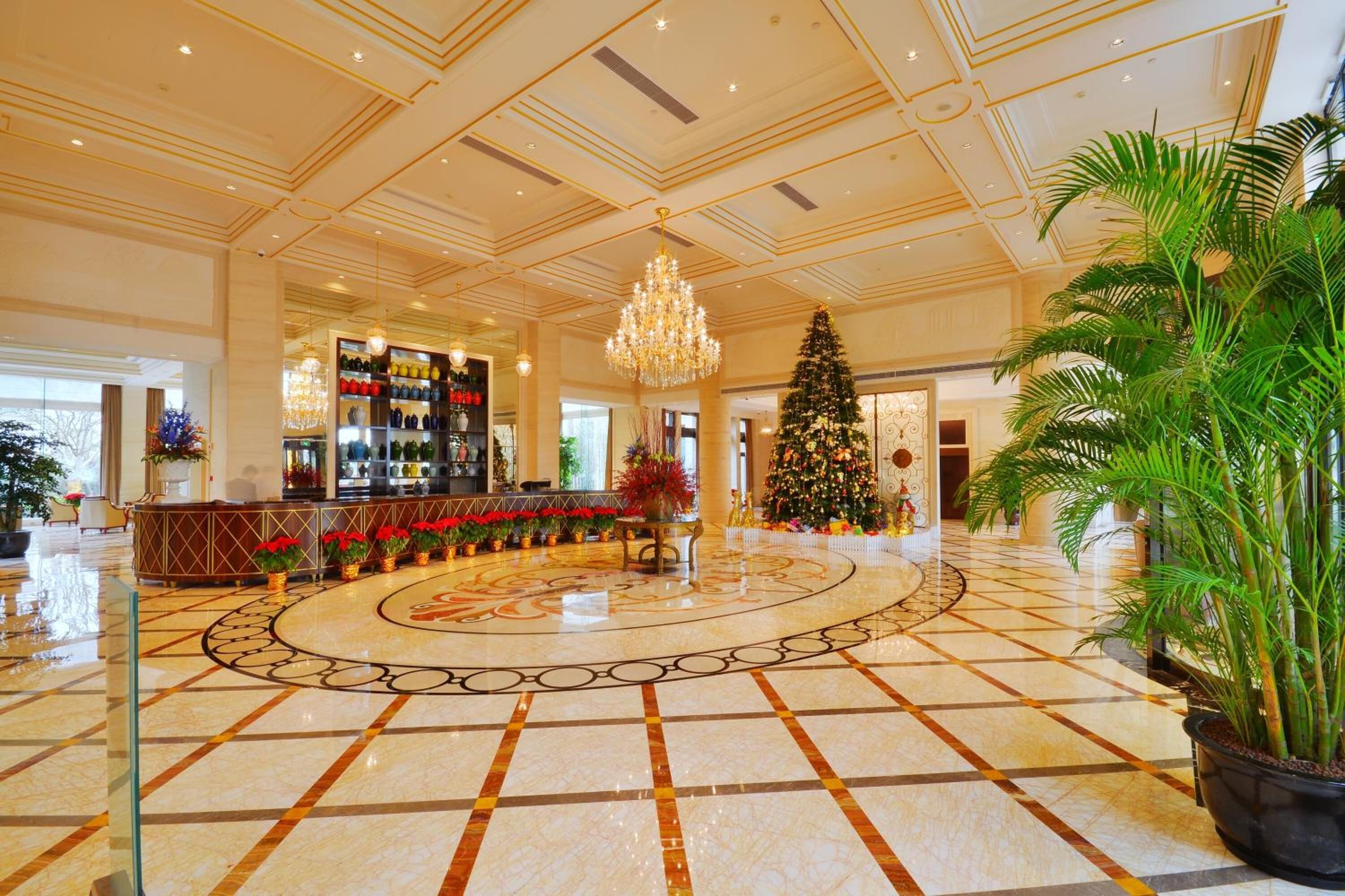 Eine geräumige Lobby mit Marmorboden, einem zentralen Chandelier, einem Weihnachtsbaum und einer Bar mit Weinauslage.