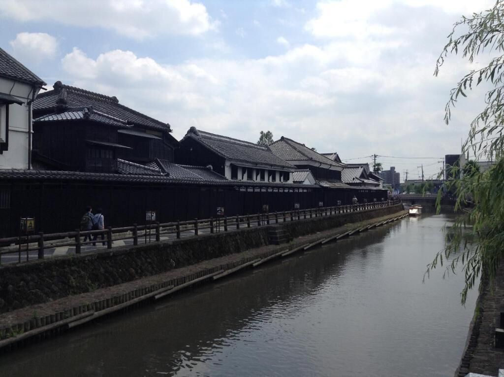 A traditional Japanese canal with buildings on one side and a bridge in the background.