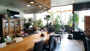 A restaurant with a wooden counter, black chairs, and potted plants. - Guest House Kuranomachi - Hostel (Tochigi)