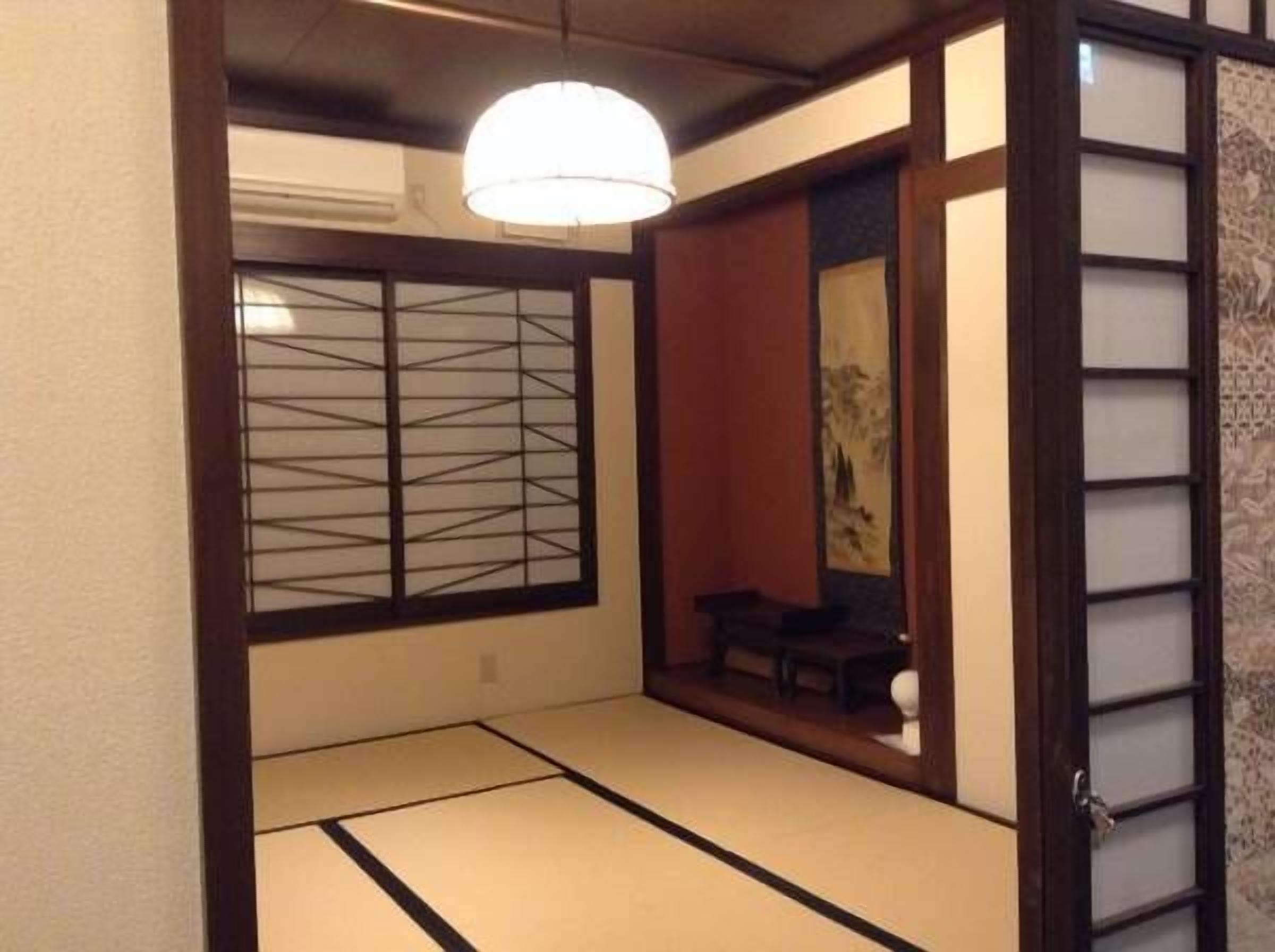 A traditional Japanese room with tatami flooring, a shoji screen, and a hanging light fixture.