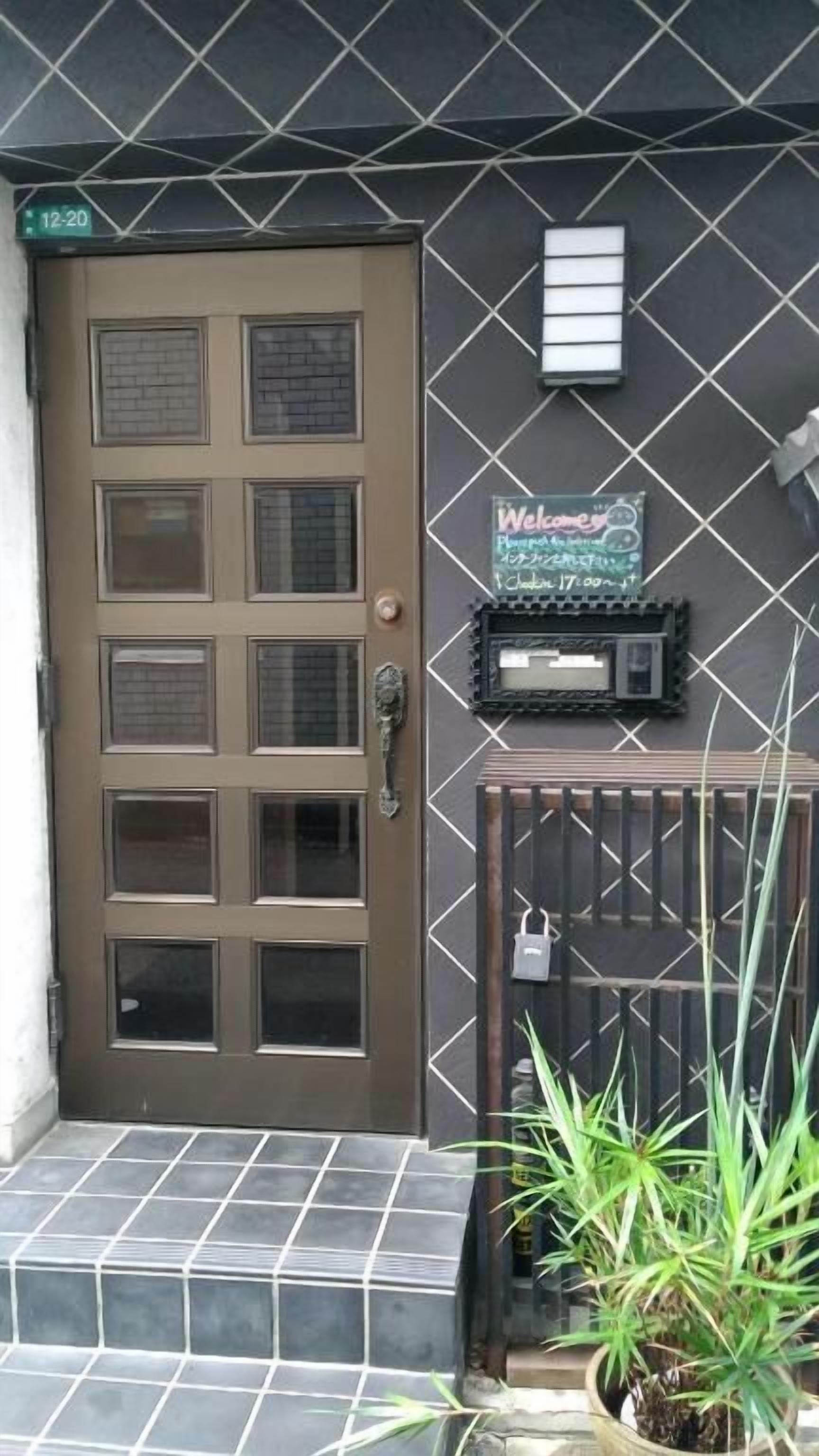 A brown door with six windows, a welcome sign, a mailbox, and a small potted plant on the steps.