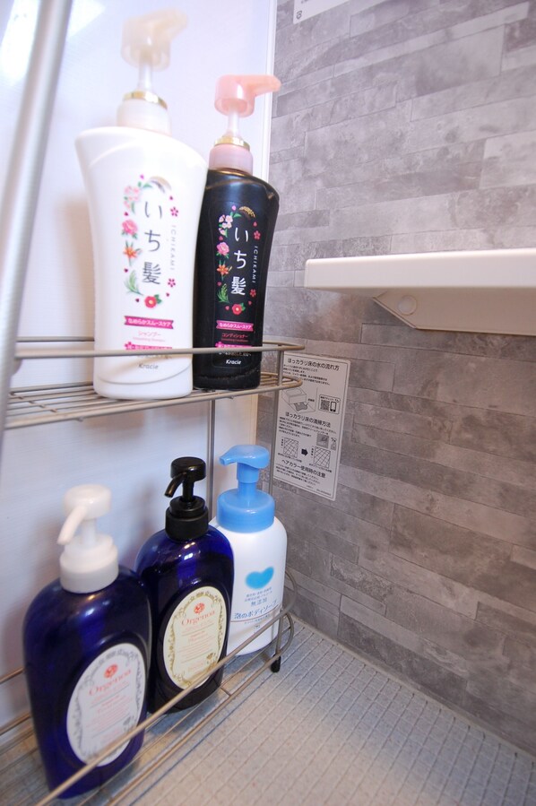 Un estante de baño con varios artículos de aseo, incluyendo una botella blanca con diseño floral, una botella negra con detalles dorados y dos botellas azules.