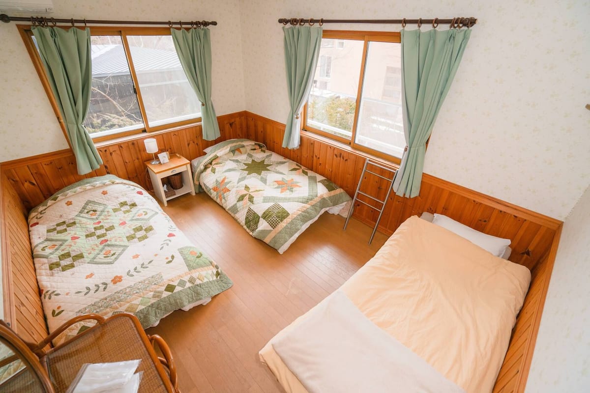 A room with two beds, a chair, a nightstand, and a window with curtains.