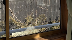 A window with a view of a wooden fence, a yellow building, and a mountain in the background. - Guesthouse Chaconne Karuizawa (Karuizawa)