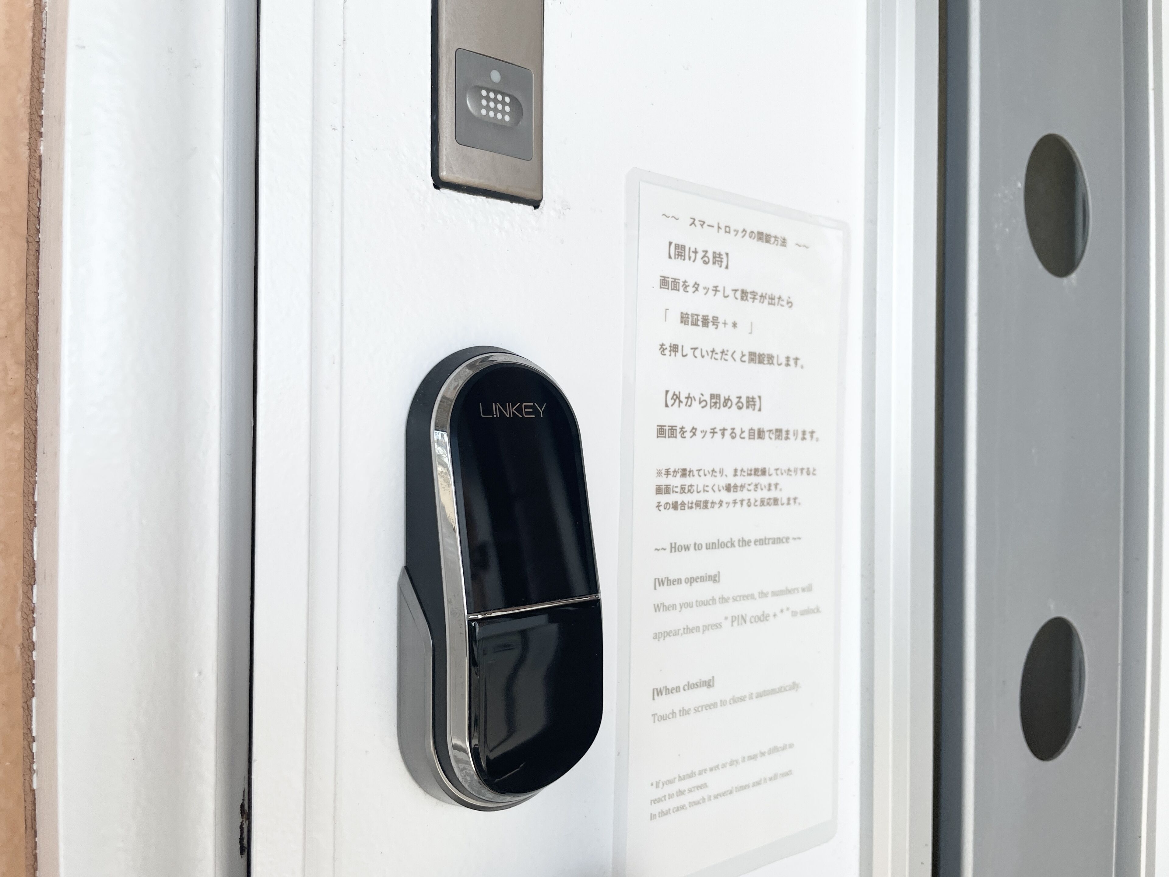 Eine Tür mit einem schwarzen 'LINKEY'-Zugangskontrollgerät und einem weißen Hinweisschild mit japanischem Text.