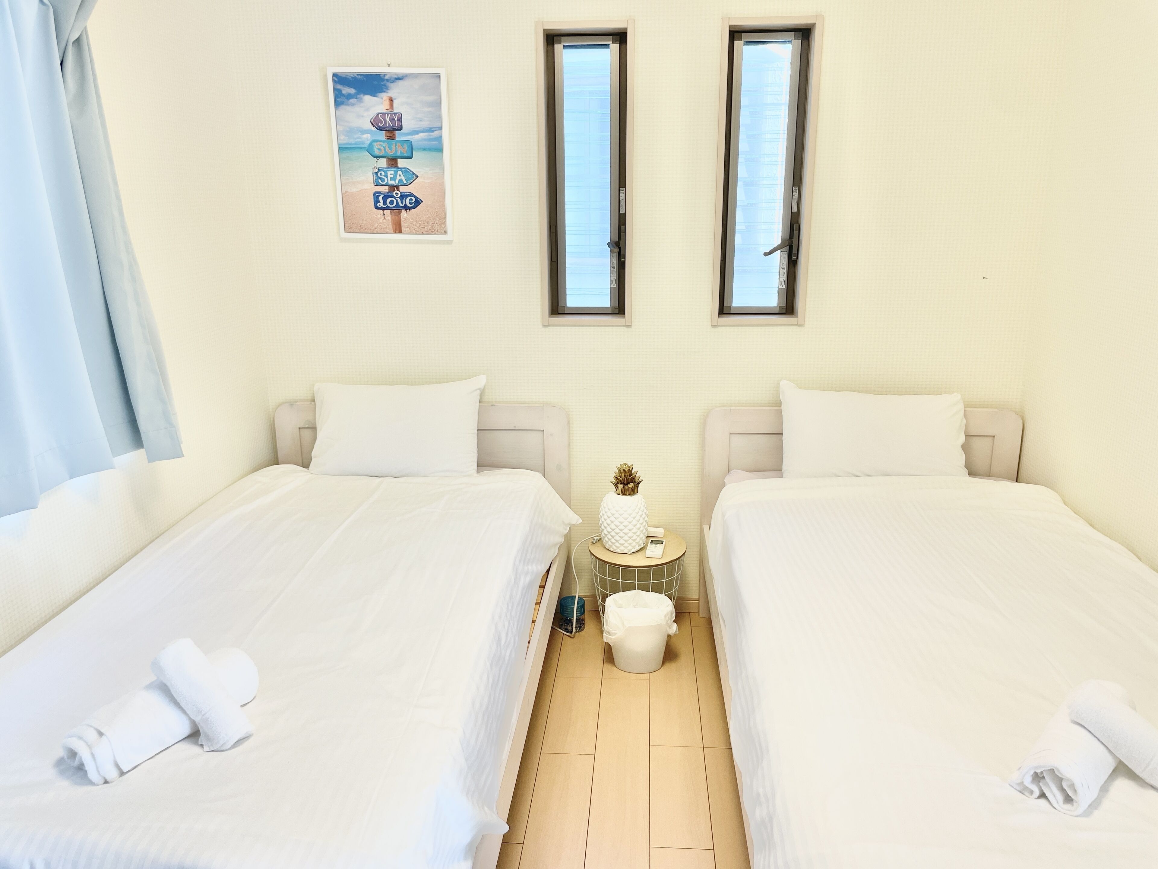 Une chambre d’hôtel avec deux lits, une petite table ronde ornée d’un vase et d’un téléphone, et un tableau accroché au mur.