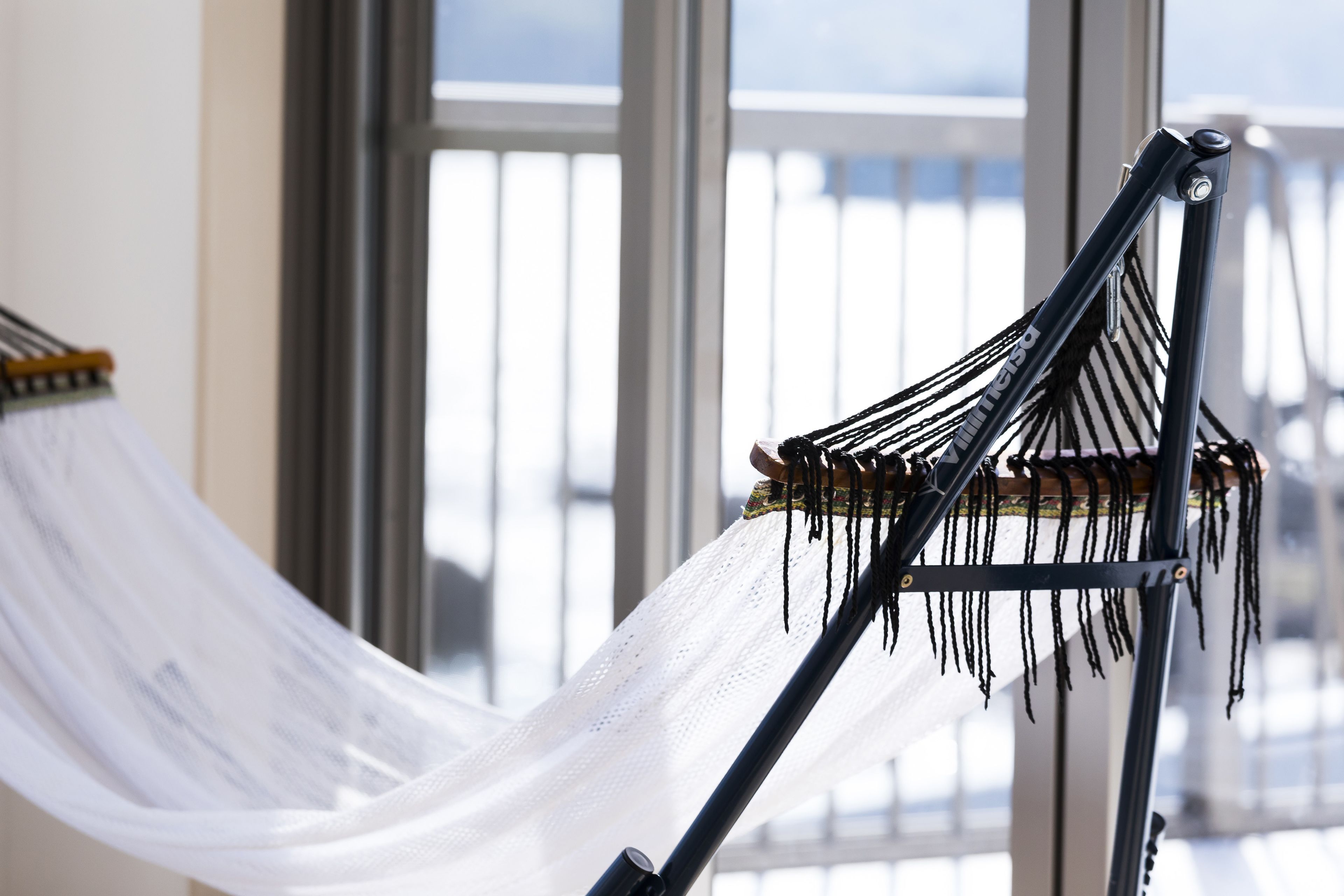 A hammock with a white net, attached to a metal frame, in a room with large windows.