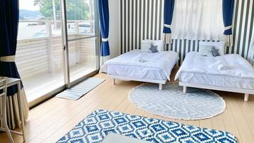 Quarto com duas camas, uma janela grande com cortinas, uma varanda e um tapete estampado.