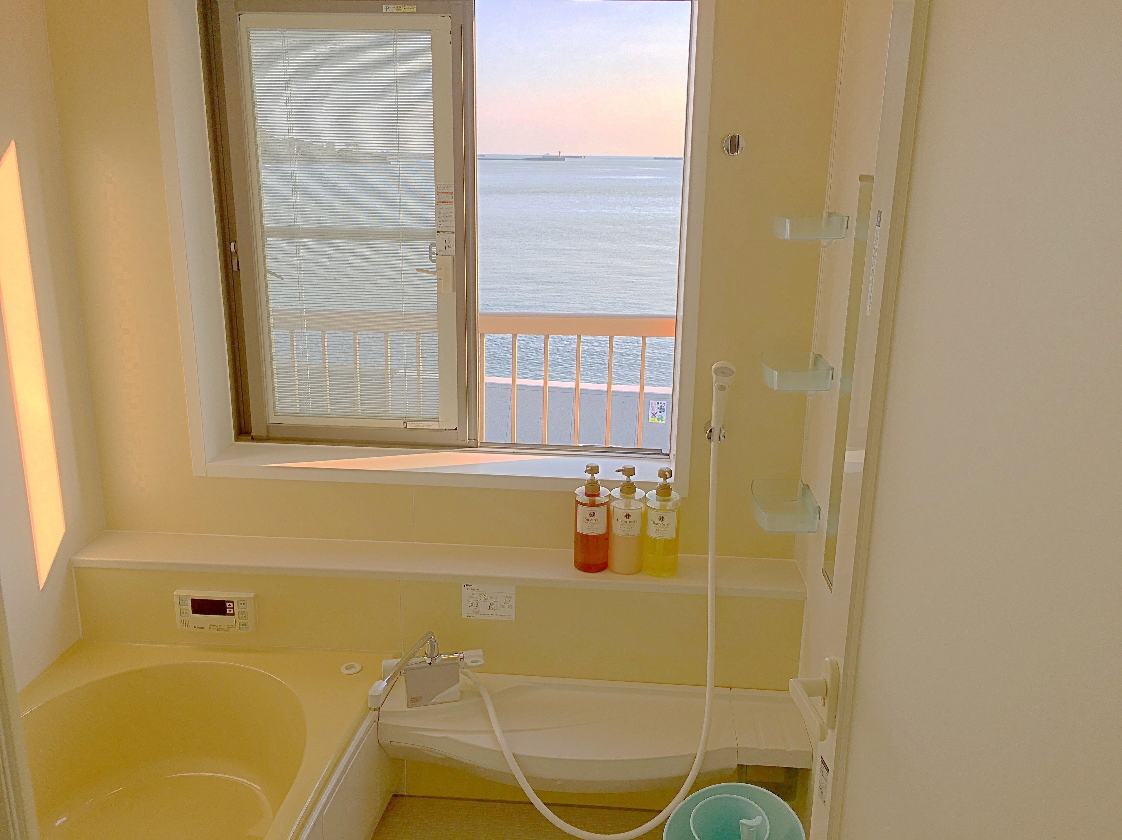 A bathroom with a bathtub, a toilet, and a window with a view of the sea.