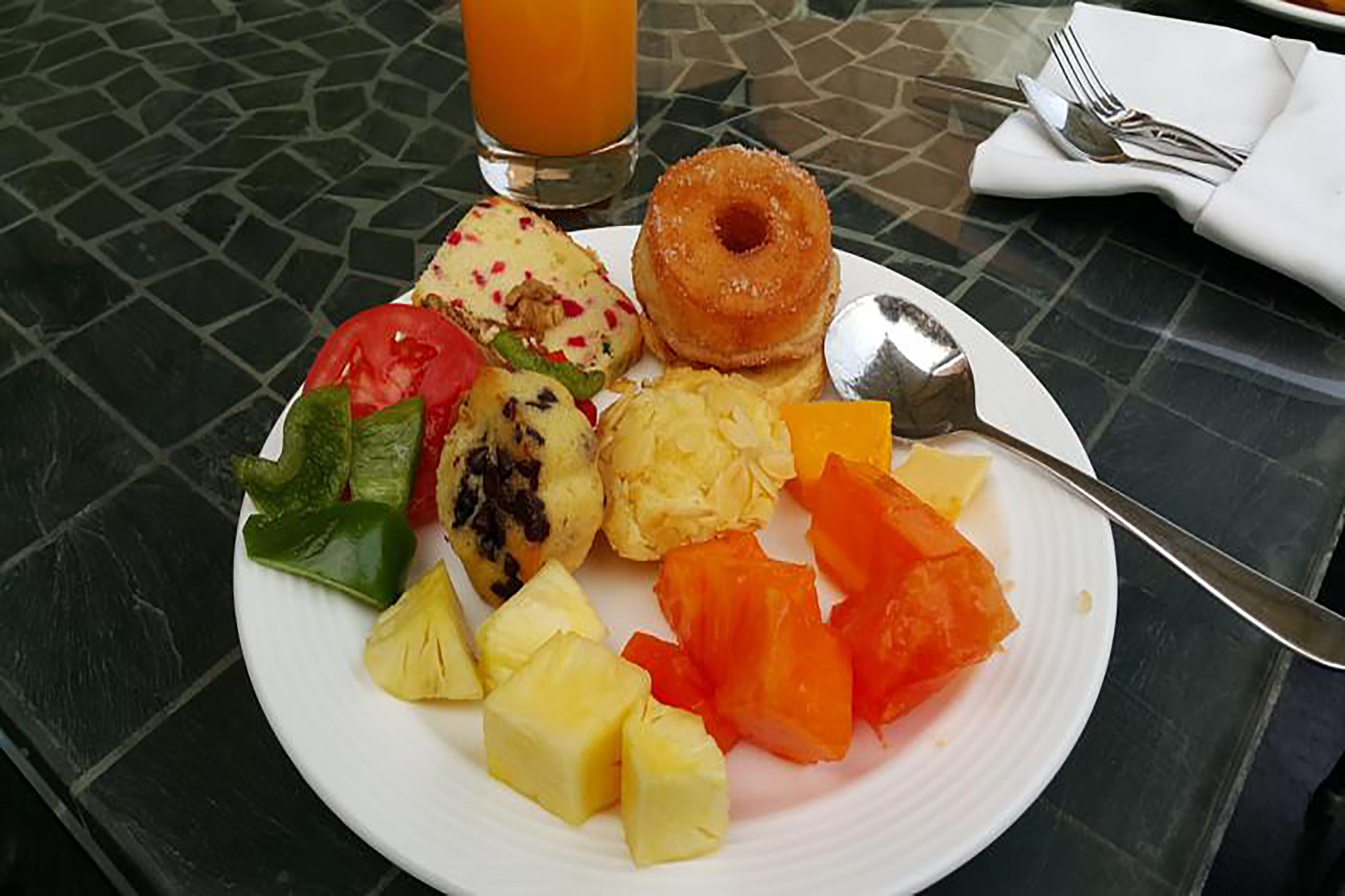 Une assiette contenant divers fruits et un verre de jus d’orange, posés sur une table.