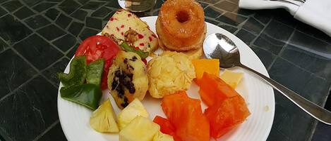 Une assiette contenant divers fruits et un verre de jus d’orange, posés sur une table.
