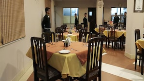 Un comedor con varias mesas, cada una cubierta con un mantel amarillo, y sillas de madera.