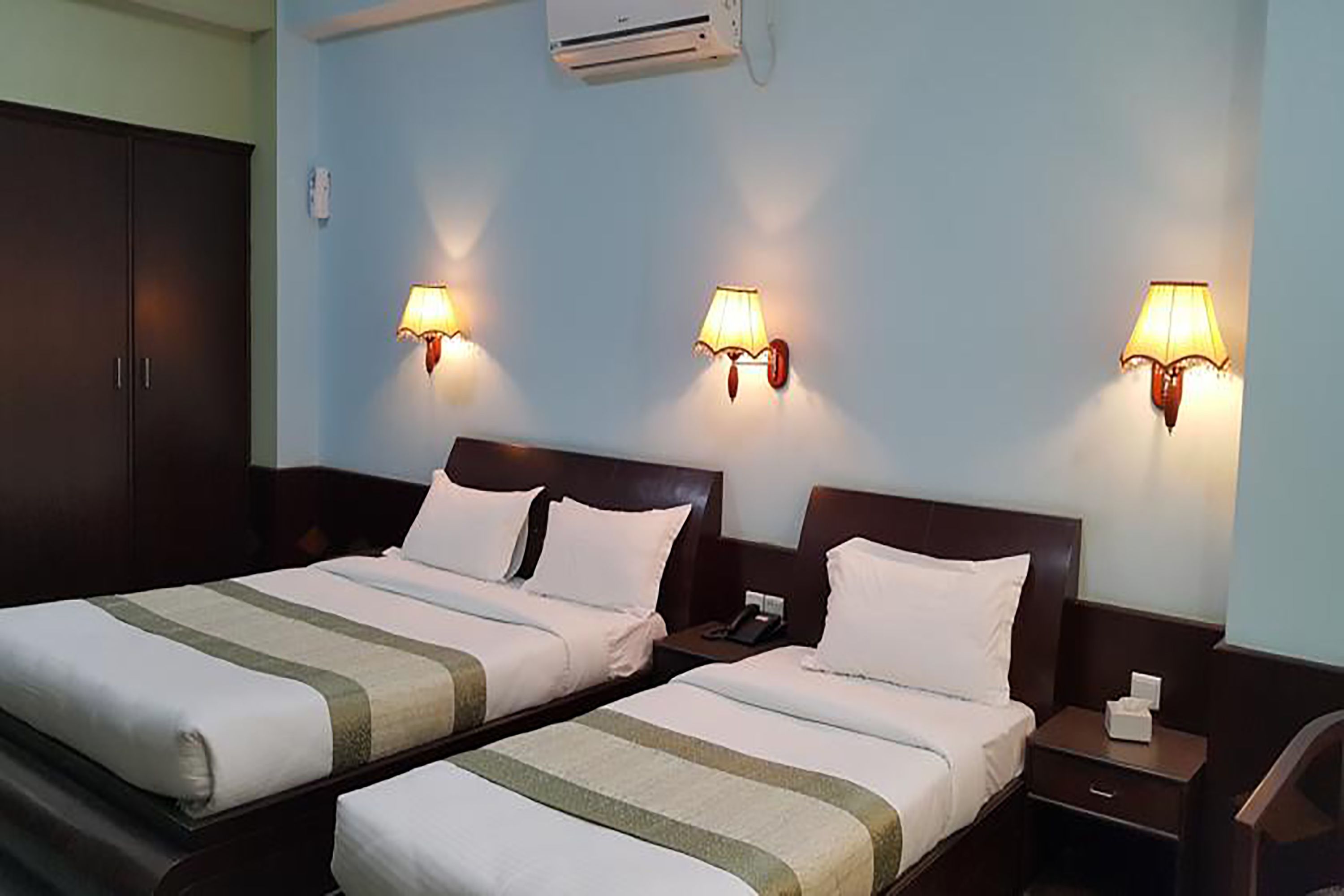 Habitación de hotel con dos camas, un armario y lámparas fijadas a la pared.