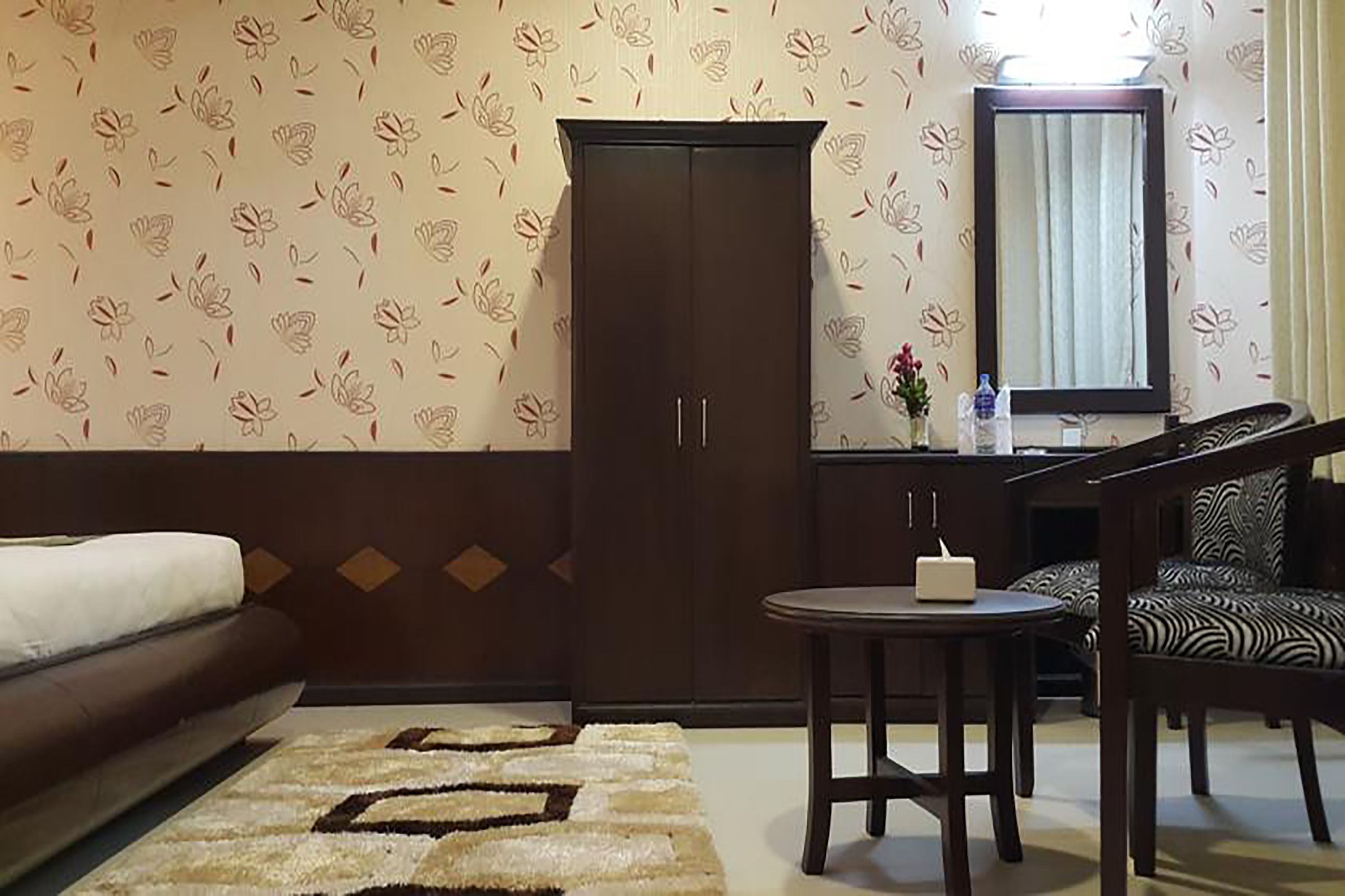 Una habitación de hotel con una cama, un armario, una mesa redonda con un jarrón y una silla.