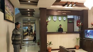 Zona de recepción con un reloj, una recepcionista y un televisor.