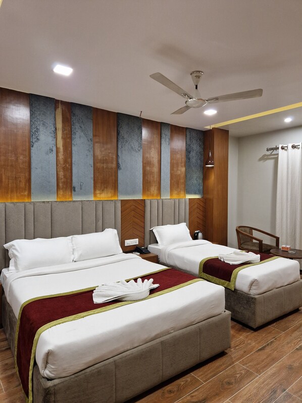 Habitación de hotel con dos camas, ventilador de techo, cabecero de madera, una mesita y una silla.