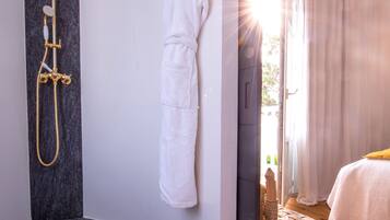 Un baño moderno con ducha dorada, bata blanca y silla de madera.