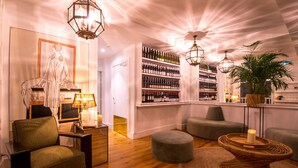 Un área de estar moderna con suelo de madera, un sillón verde, un sofá gris, una mesa redonda de mimbre con una vela y una pared de botellas de vino.