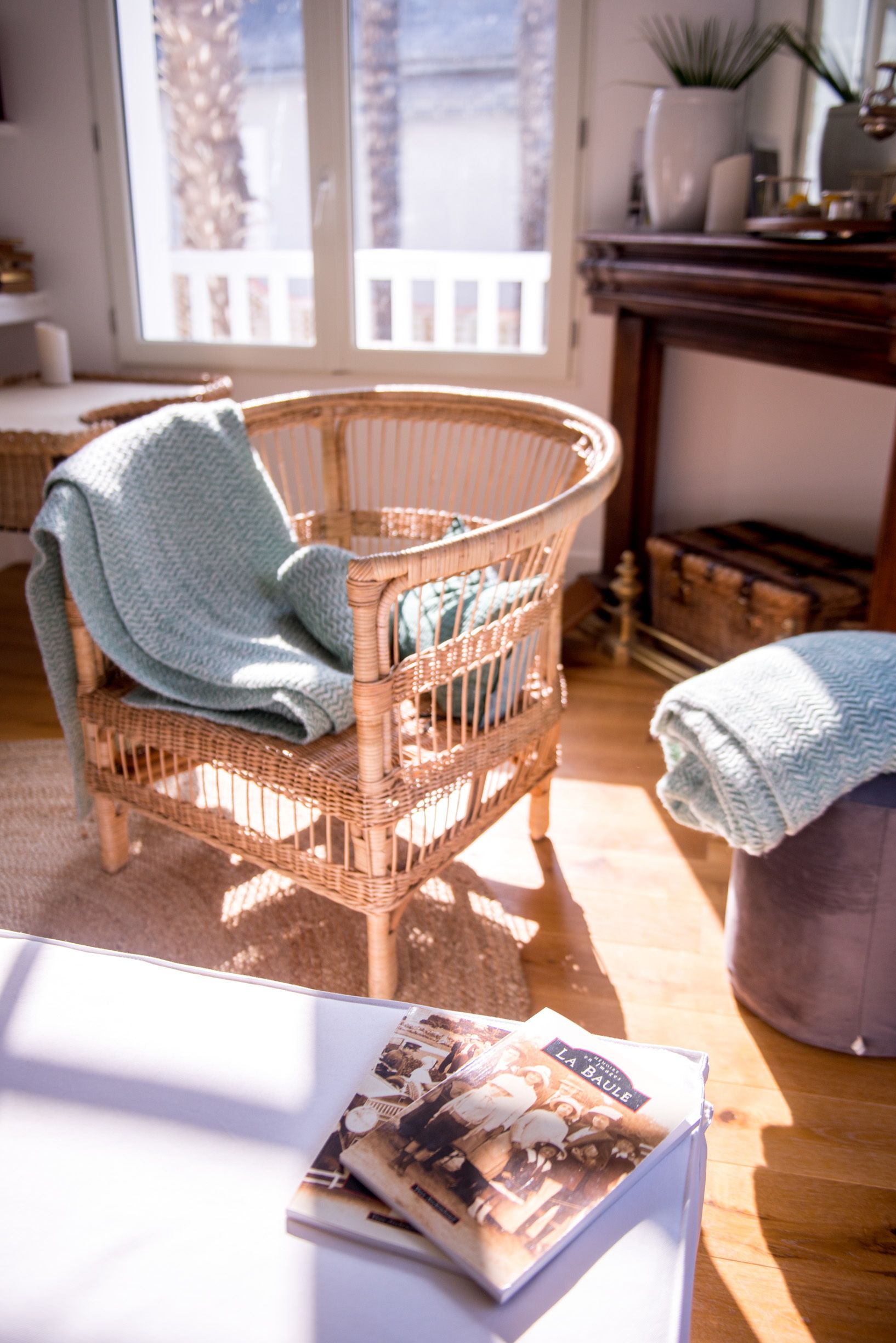 A wicker chair with a blue blanket, a table with magazines, and a wooden floor.