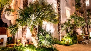 Un edificio bien iluminado con un patio empedrado, palmeras y una zona de estar.