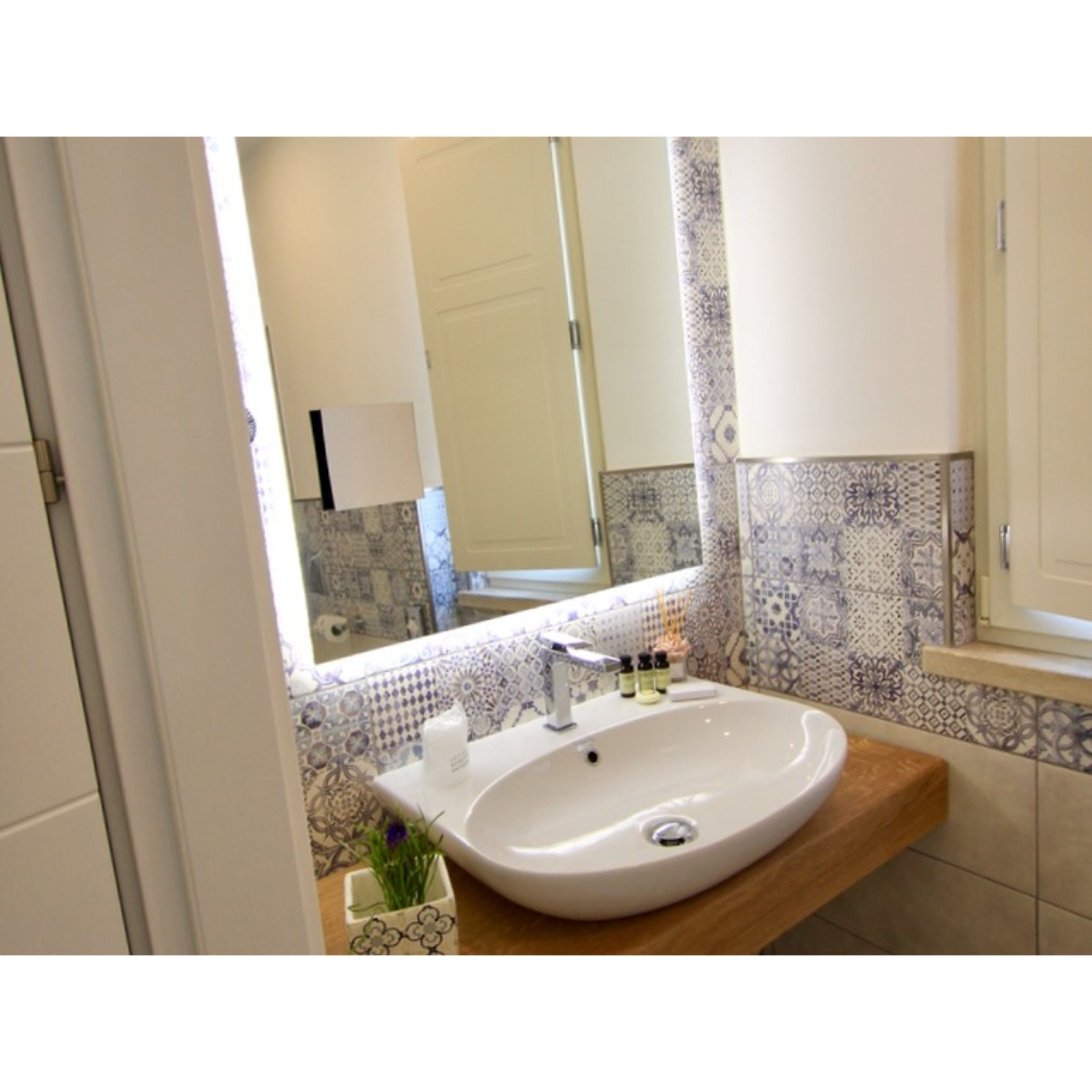Un baño con un lavamanos blanco, un espejo y azulejos estampados.