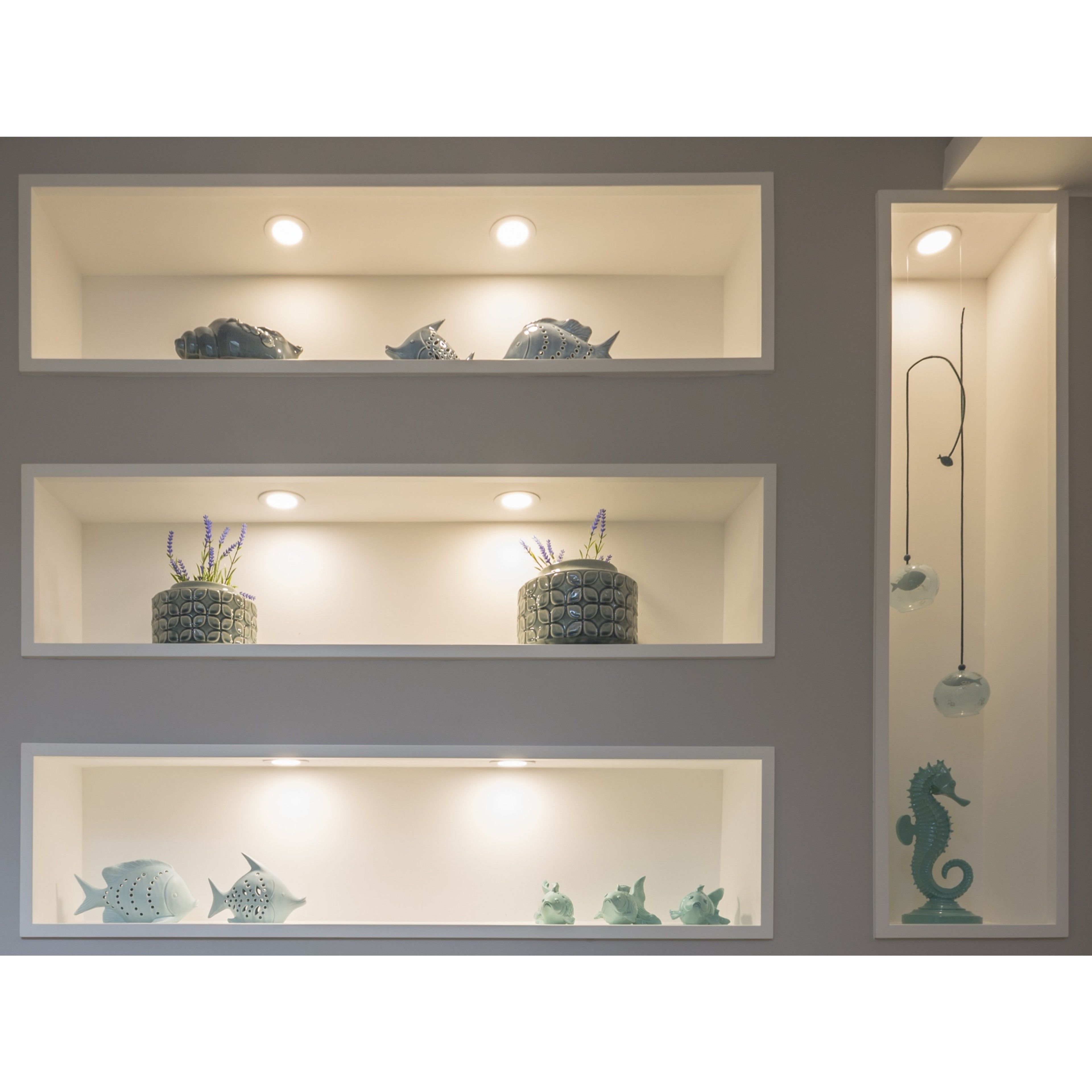 Três prateleiras com objetos decorativos, cada uma iluminada por uma luminária no teto.