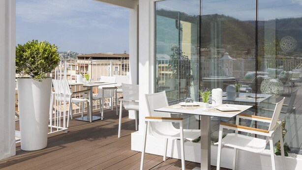 A modern outdoor seating area with white furniture and a glass partition, overlooking a scenic hillside view. - Townhouse Tropea (Tropea)