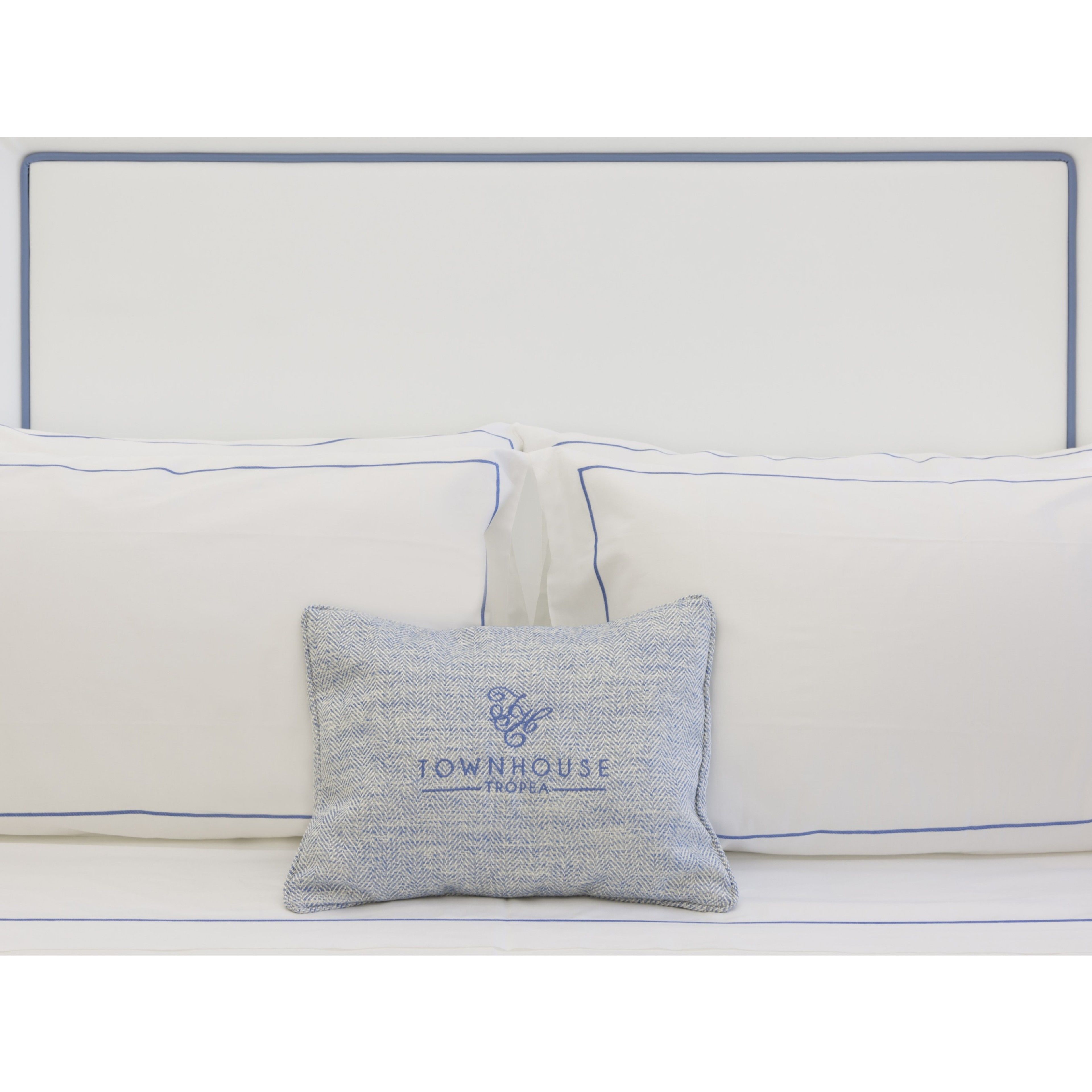 A white sofa with blue piping and a single grey pillow with embroidered text.