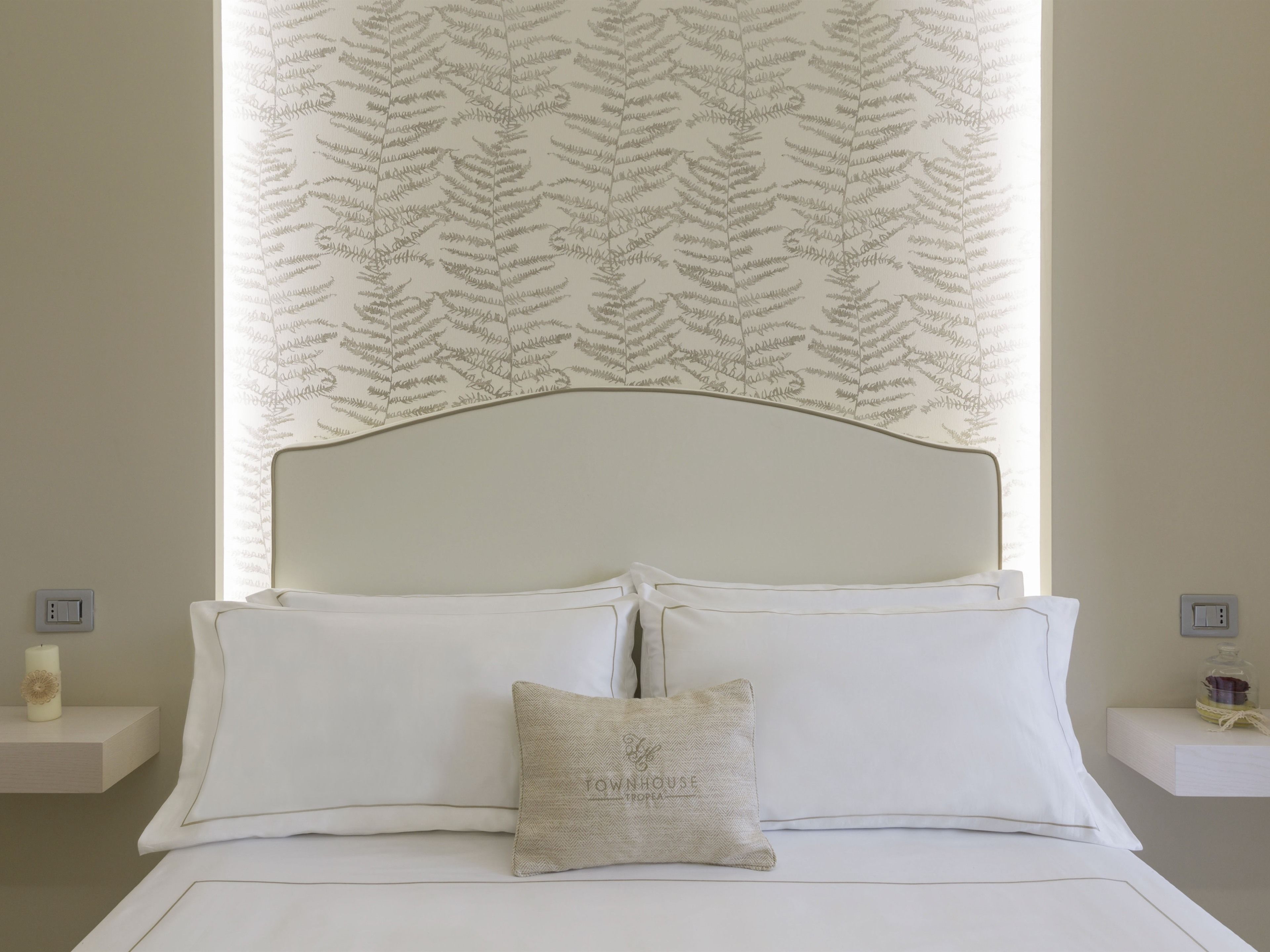 A neatly made bed with white linens, a single decorative pillow, and a headboard.