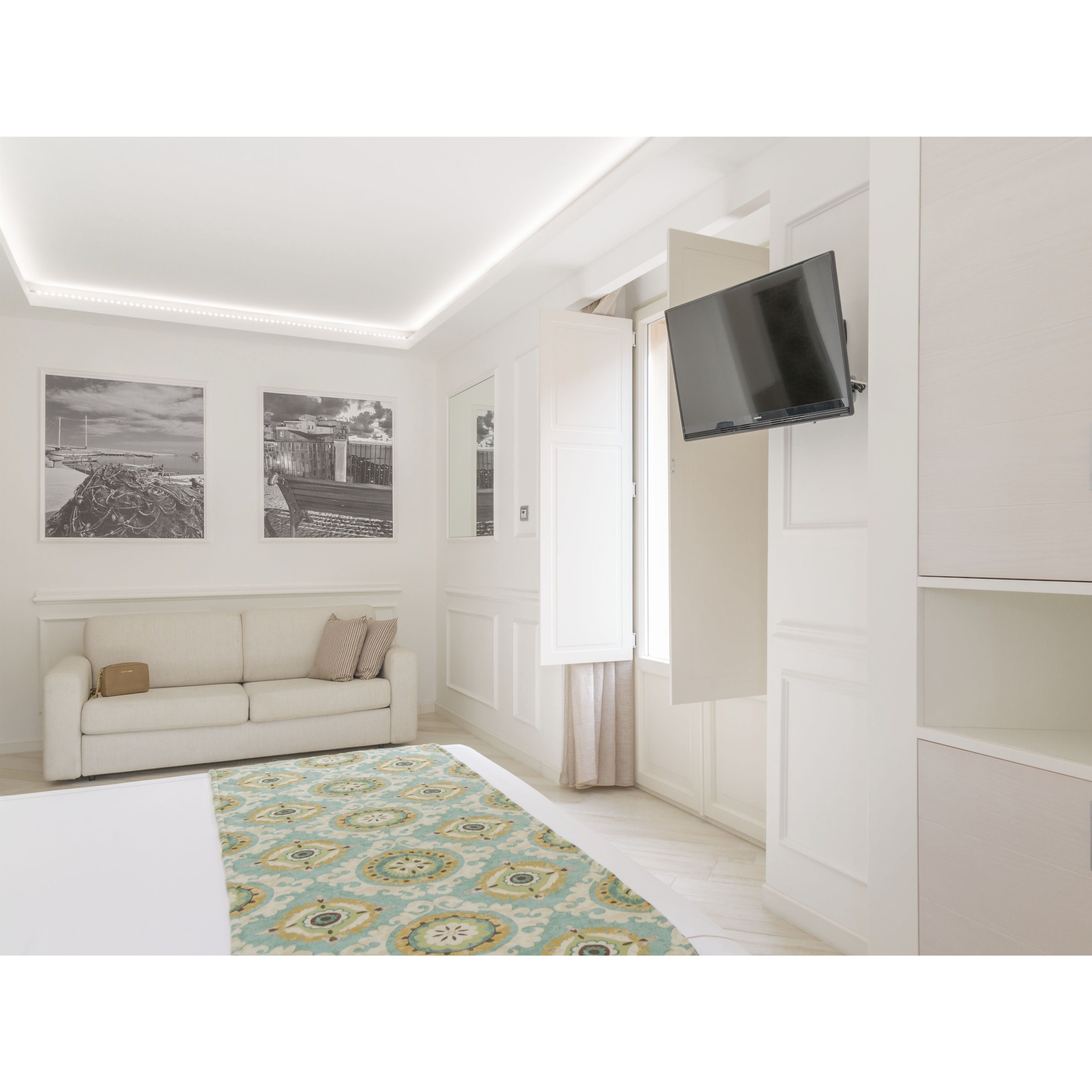 A modern bedroom with a white sofa, a patterned rug, and a flat-screen TV mounted on the wall.