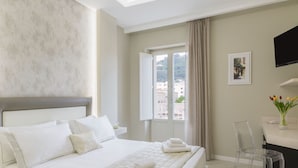 A hotel room with a large bed, a clear glass chair, a flat-screen TV, and a window with a view of buildings. - Townhouse Tropea (Tropea)