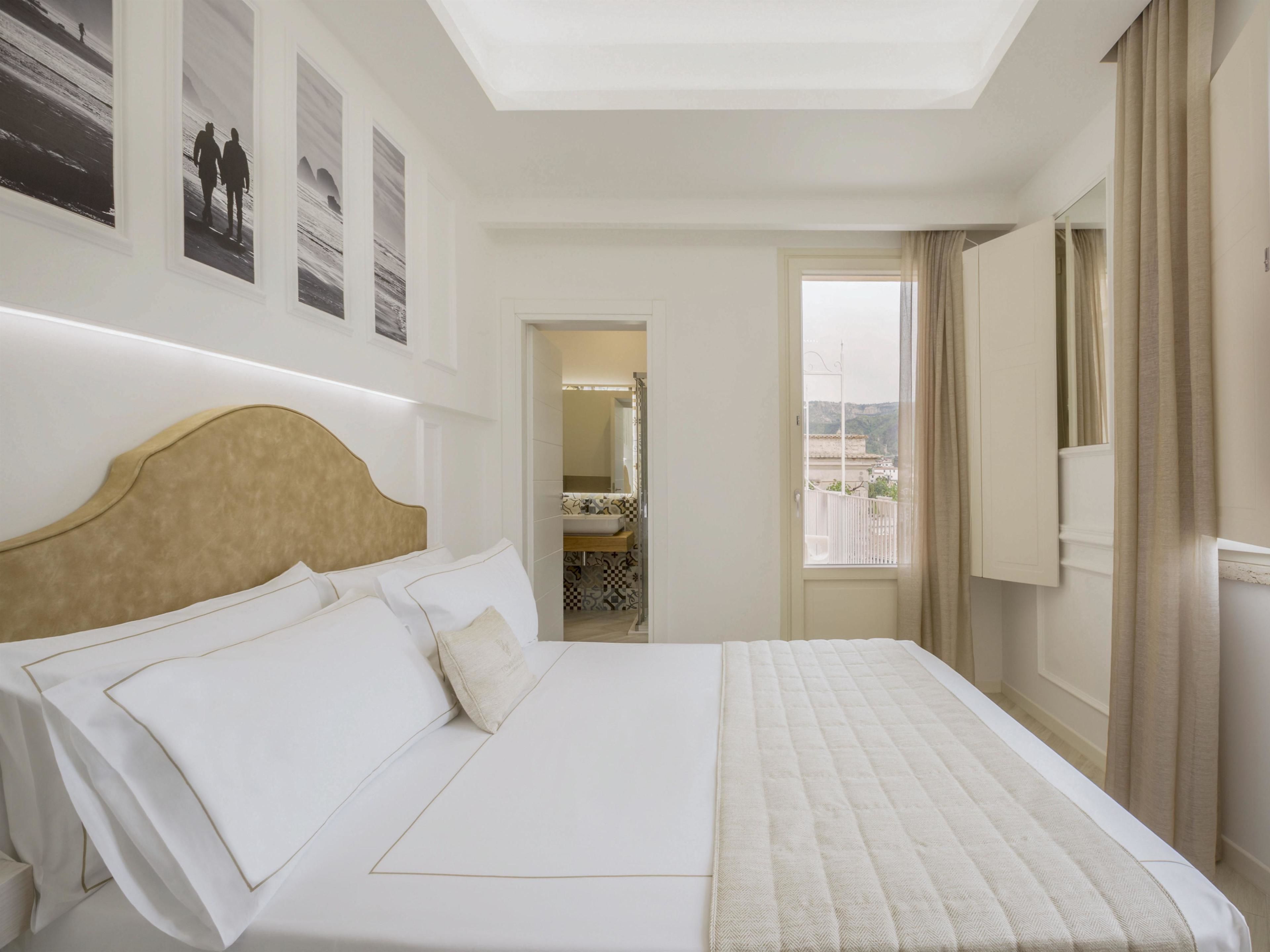 Ein Hotelzimmer mit einem großen Bett, einem Kopfteil, einem Fenster mit Vorhängen und Blick auf die Stadt.