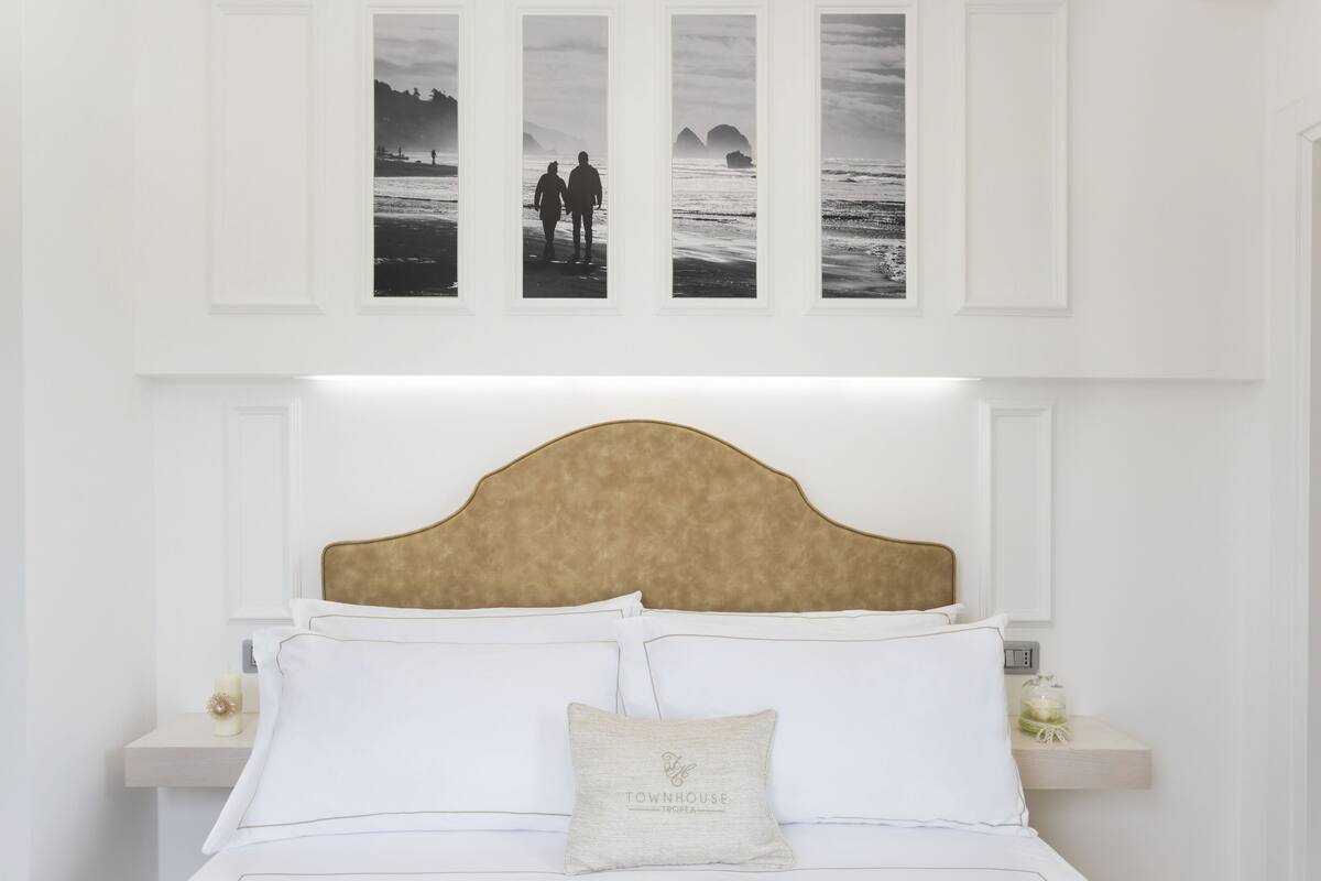 A bedroom with a large bed, a headboard, bedside tables, and wall-mounted artwork depicting a beach scene.