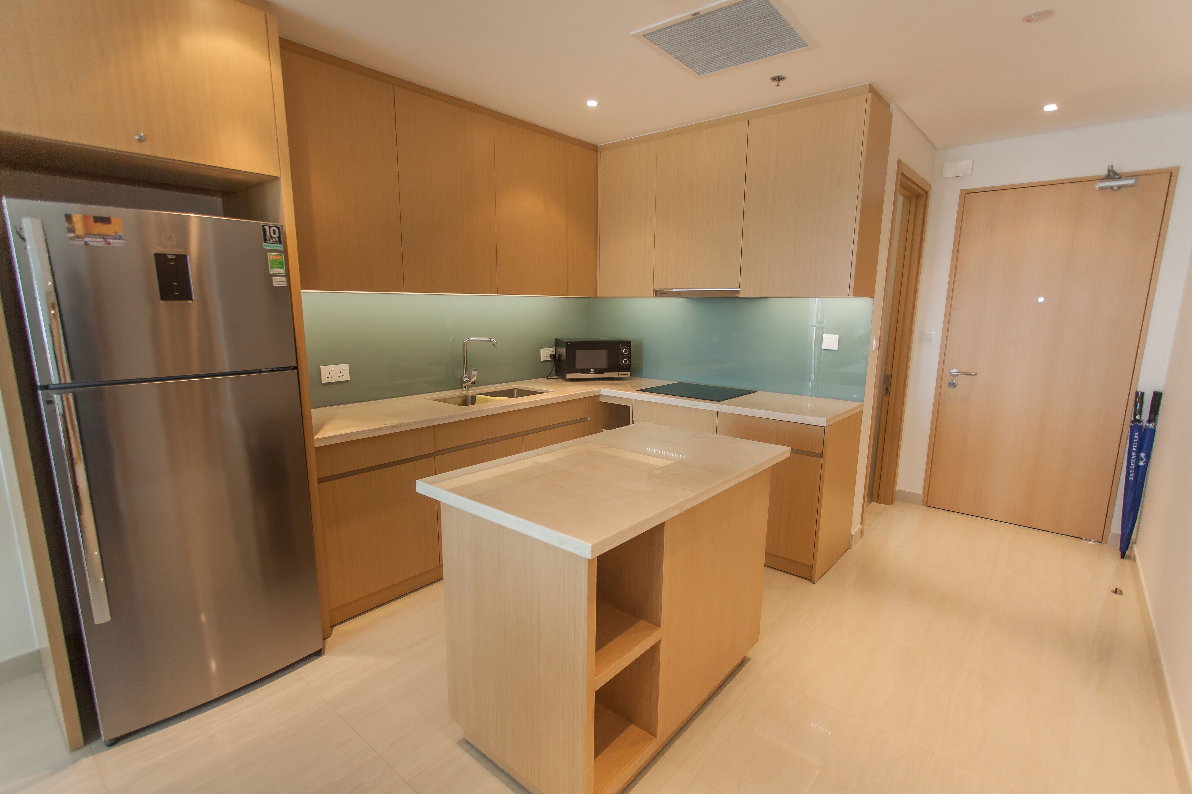 A modern kitchen with wooden cabinets, a stainless steel refrigerator, a microwave, and a sink.