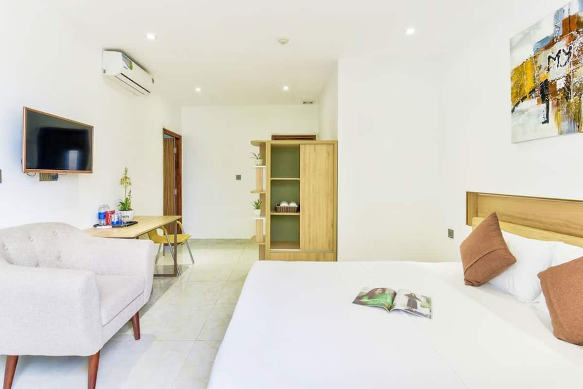 A hotel room with a bed, a desk, a chair, a TV, and a bookshelf.