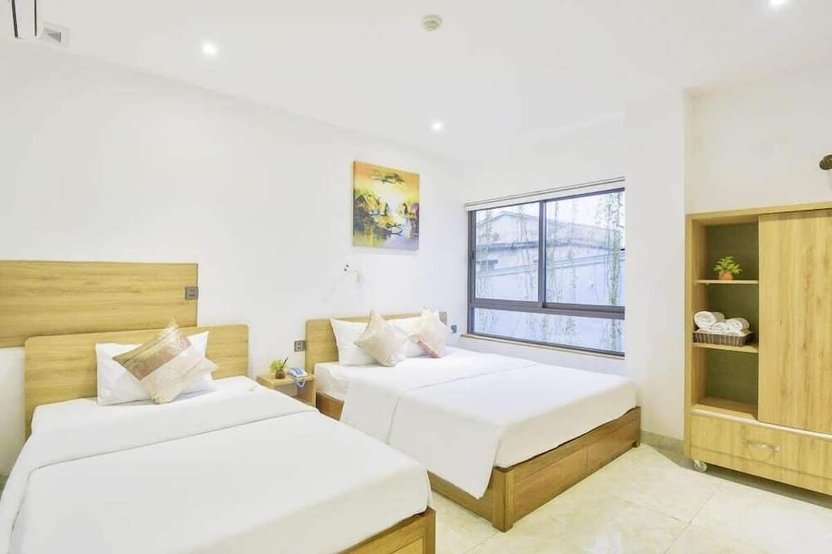 A hotel room with two beds, a window, a painting, and a wooden wardrobe.