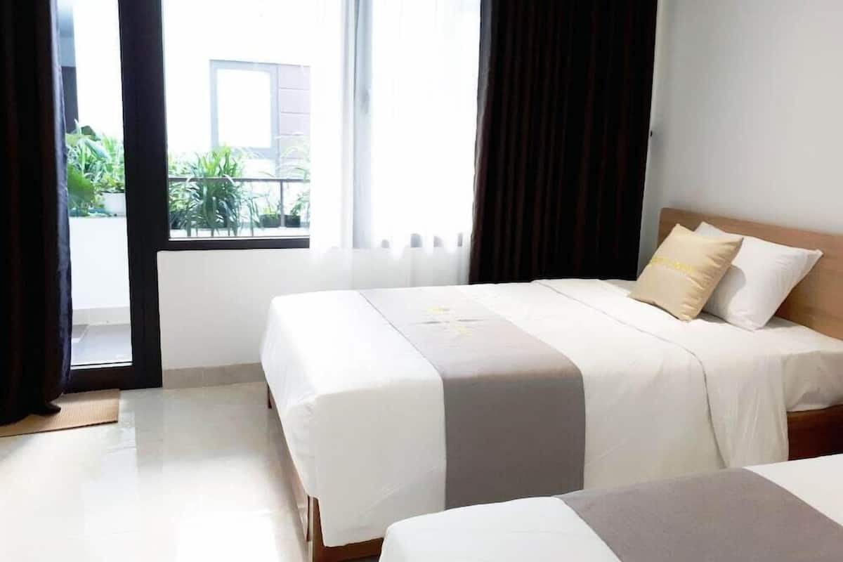 A hotel room with a bed, a window with curtains, and a view of greenery outside.