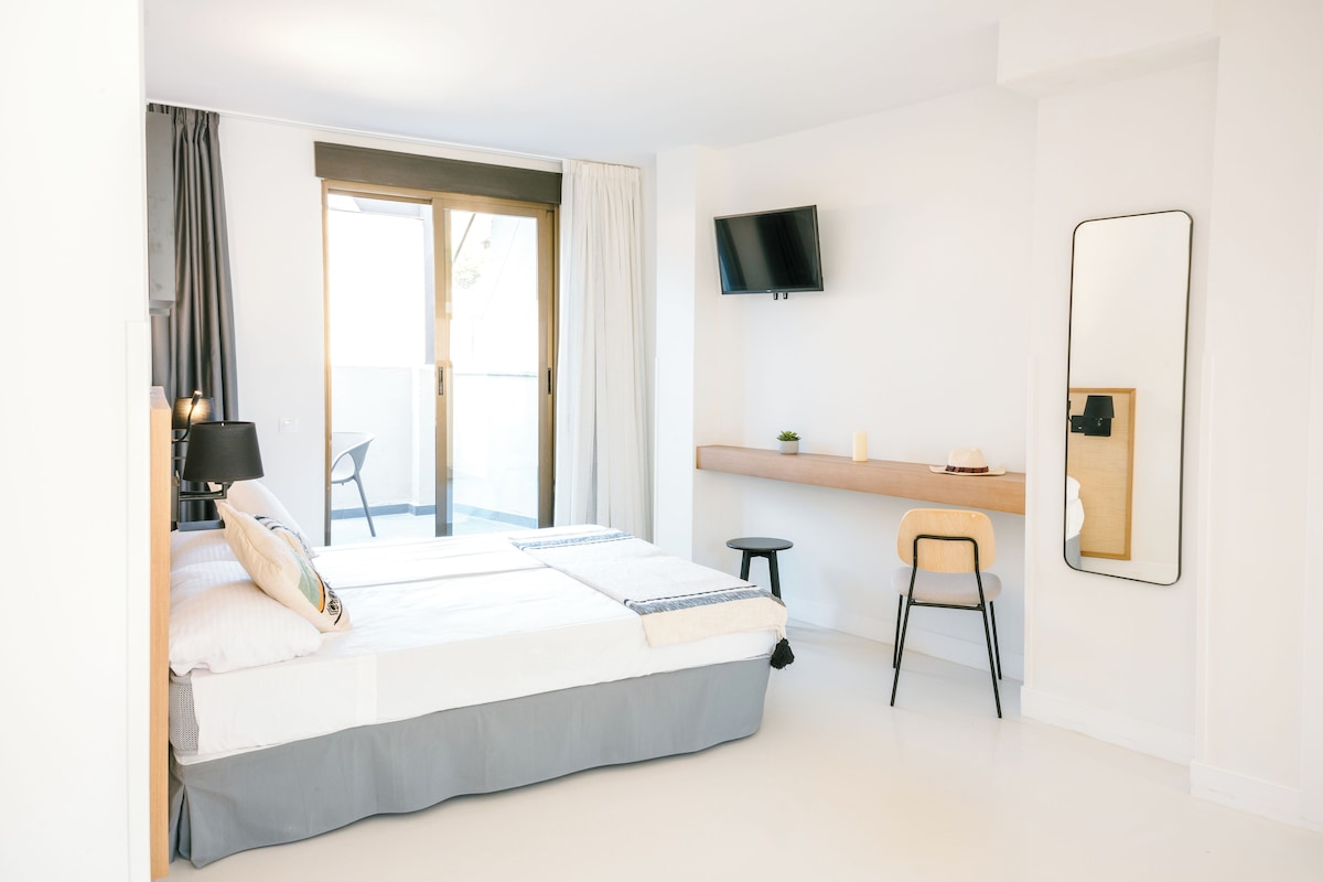 A modern hotel room with a bed, a desk, a chair, a TV, and a large mirror.