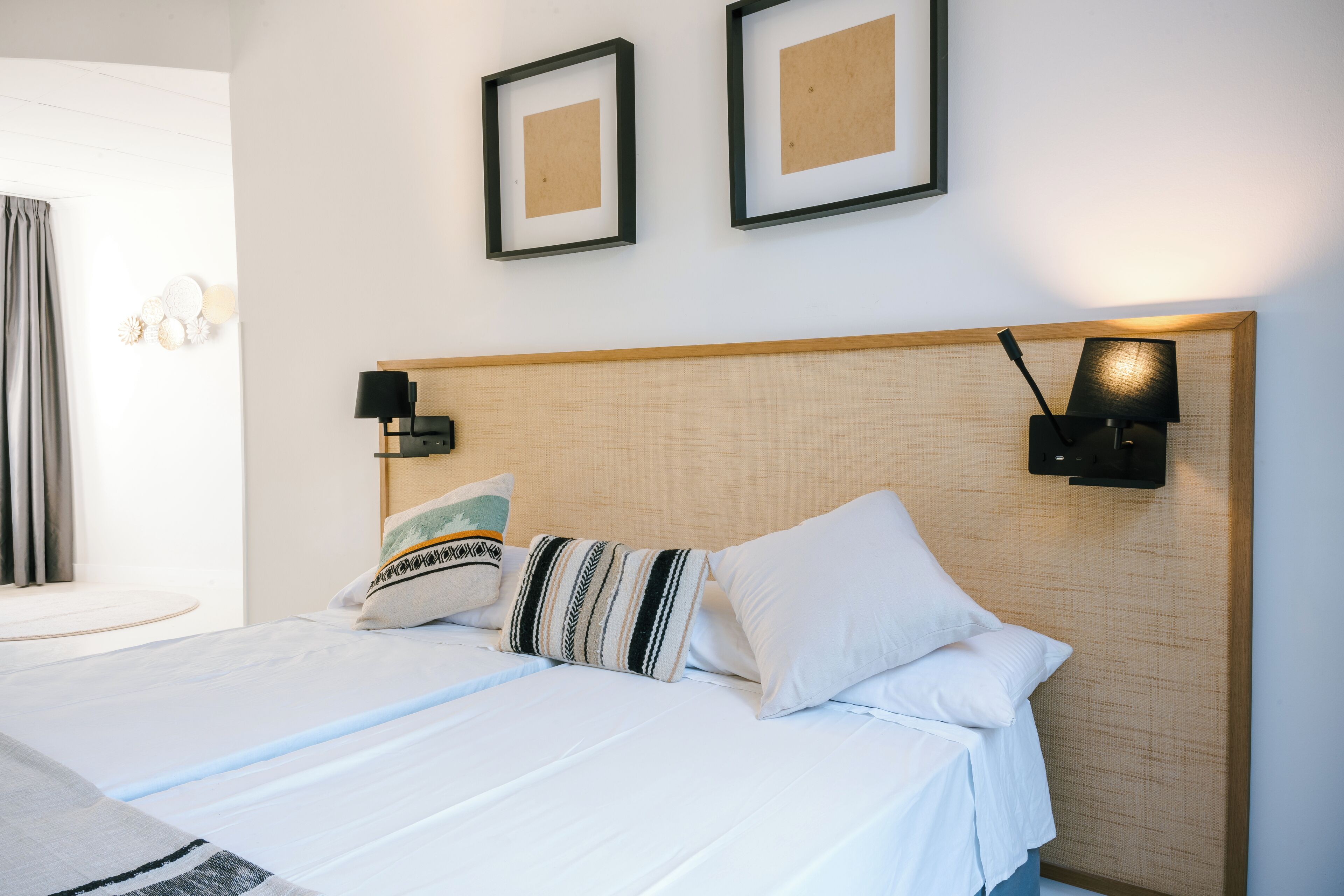 Un lit bien fait, avec du linge de lit blanc et des oreillers à rayures, une tête de lit en bois et deux tableaux encadrés accrochés au mur.