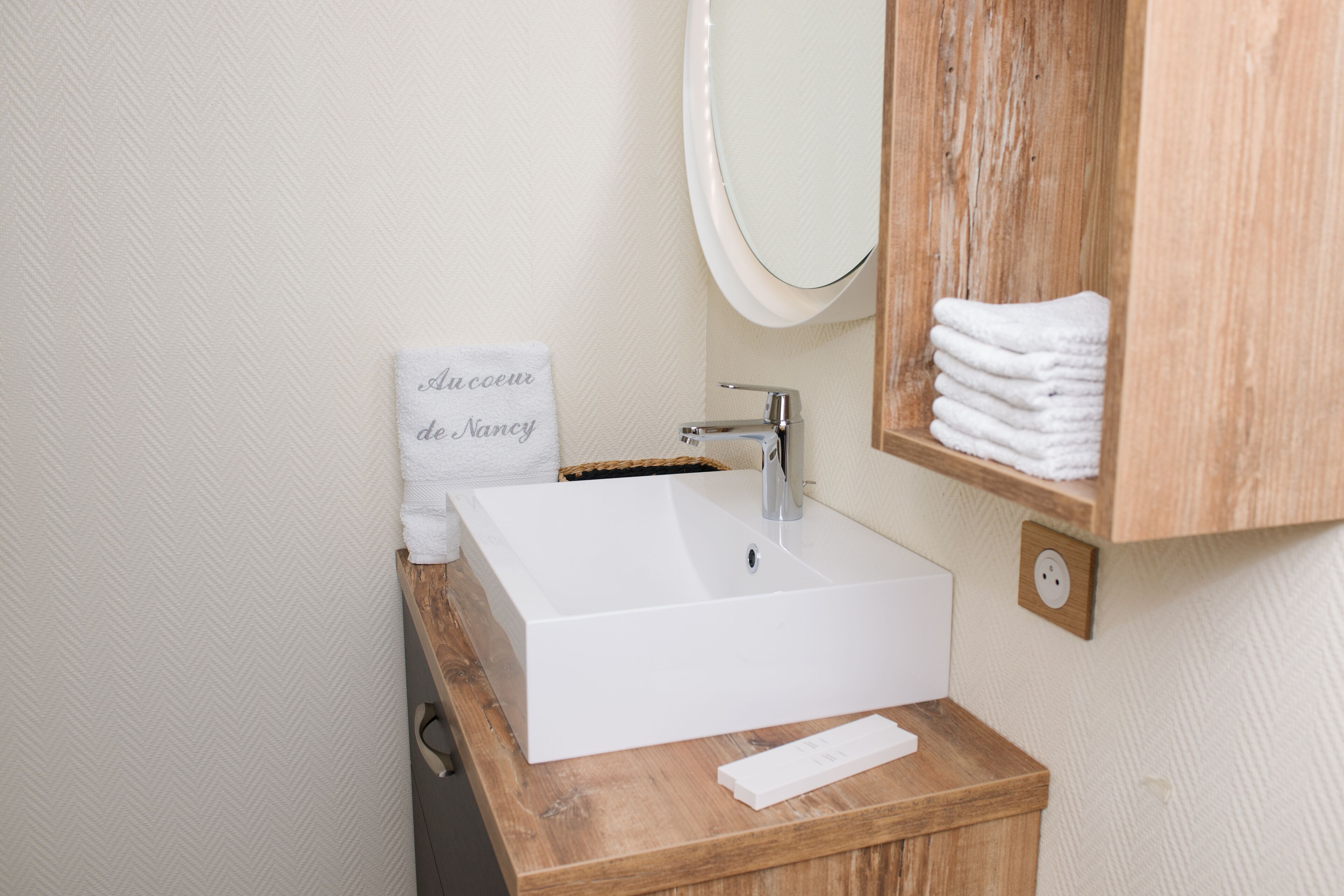Une salle de bain avec un lavabo blanc, un meuble-lavabo en bois, un miroir et un porte-serviettes avec des serviettes pliées.