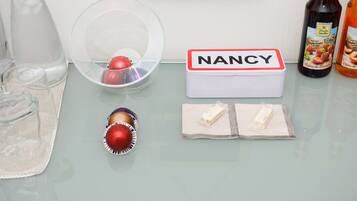 Ein Tisch mit einer klaren Plastikschale, einer weißen Schachtel mit dem Aufdruck 'NANCY', einem kleinen roten Gegenstand und zwei Päckchen weißem Pulver.